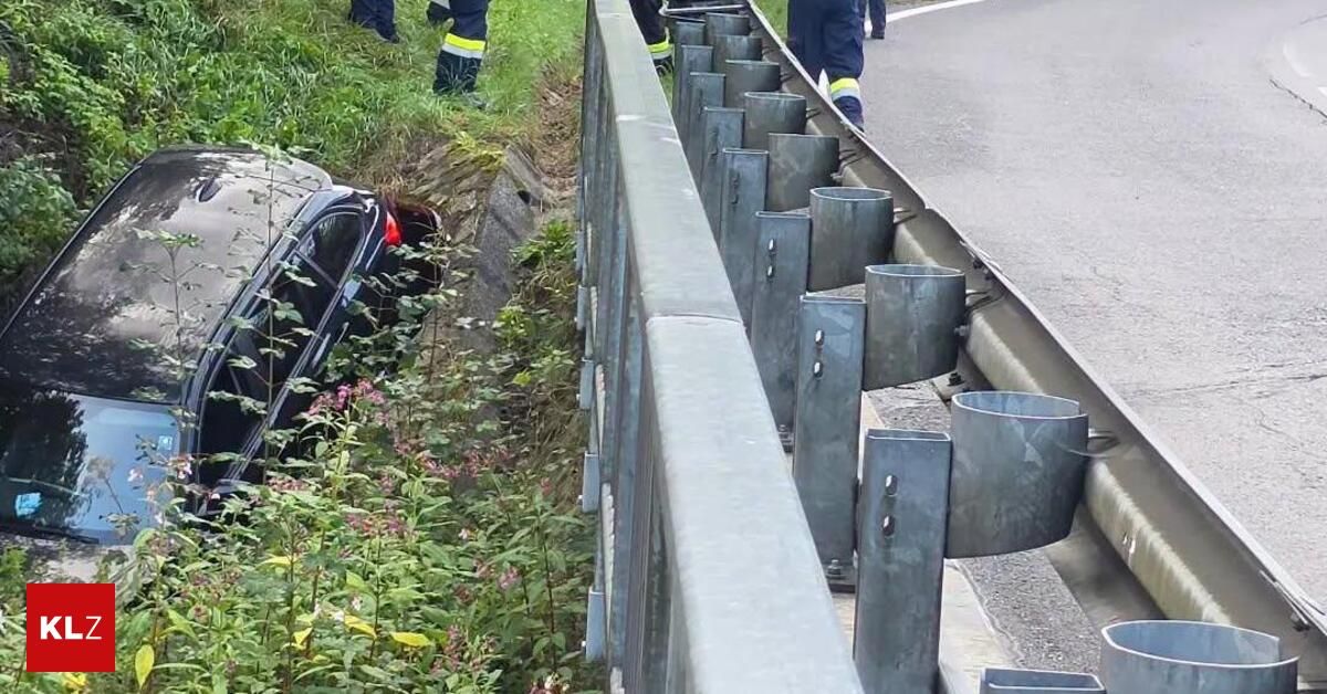 Ein Auto ist teilweise von der Straße abgekommen und lehnt sich gegen eine Betonbarriere mit Metallpfosten. Rettungskräfte sind anwesend.