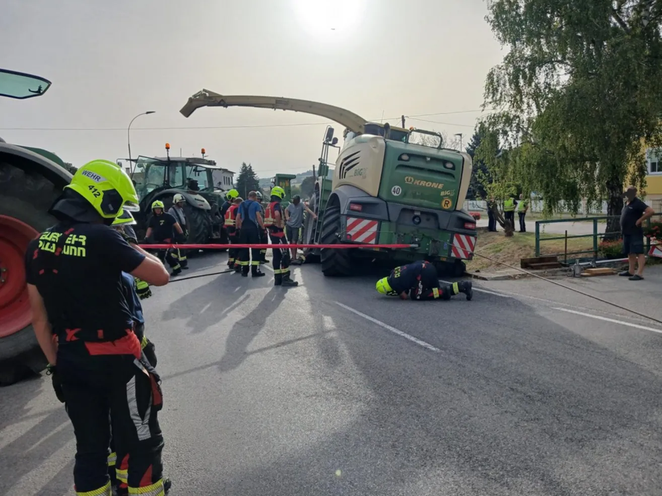 Einsatzkräfte in gelben Helmen stehen um einen großen grünen Traktor am Straßenrand, ein Arbeiter liegt auf dem Boden.