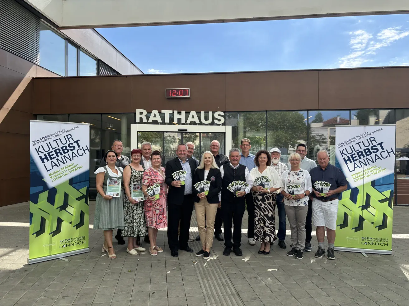 Eine Gruppe von Menschen steht vor einem Gebäude mit einem Schild, das Rathaus besagt. Sie halten Broschüren und posieren für ein Foto.