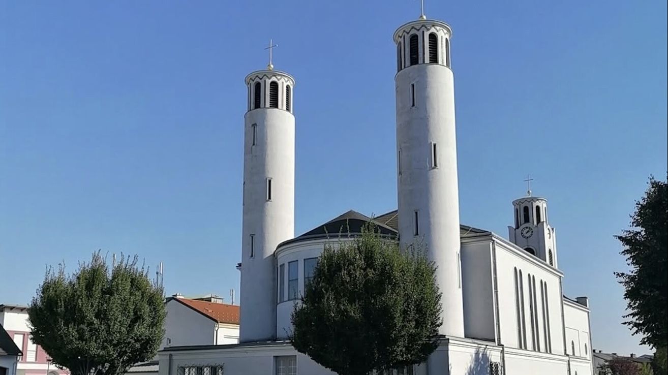 Eine weiße Kirche mit zwei hohen Türmen, einer mit einem Kreuz oben, unter einem klaren blauen Himmel.