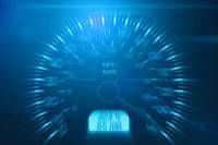 Ein Tachometer mit blauem Hintergrund und leuchtenden blauen Zahlen, die die Geschwindigkeit anzeigen. Der Zeiger zeigt auf eine hohe Geschwindigkeit.