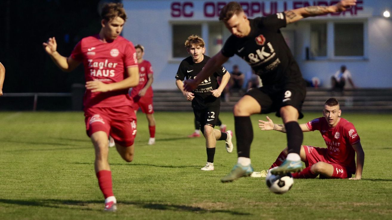 Fußballspieler in Aktion auf einem Feld, einer in Rot und einer in Schwarz, mit einem Fußball auf dem Boden.