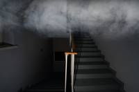 Eine Treppe mit einem Geländer führt in eine Rauchwolke hinab und schafft eine dramatische und geheimnisvolle Atmosphäre.