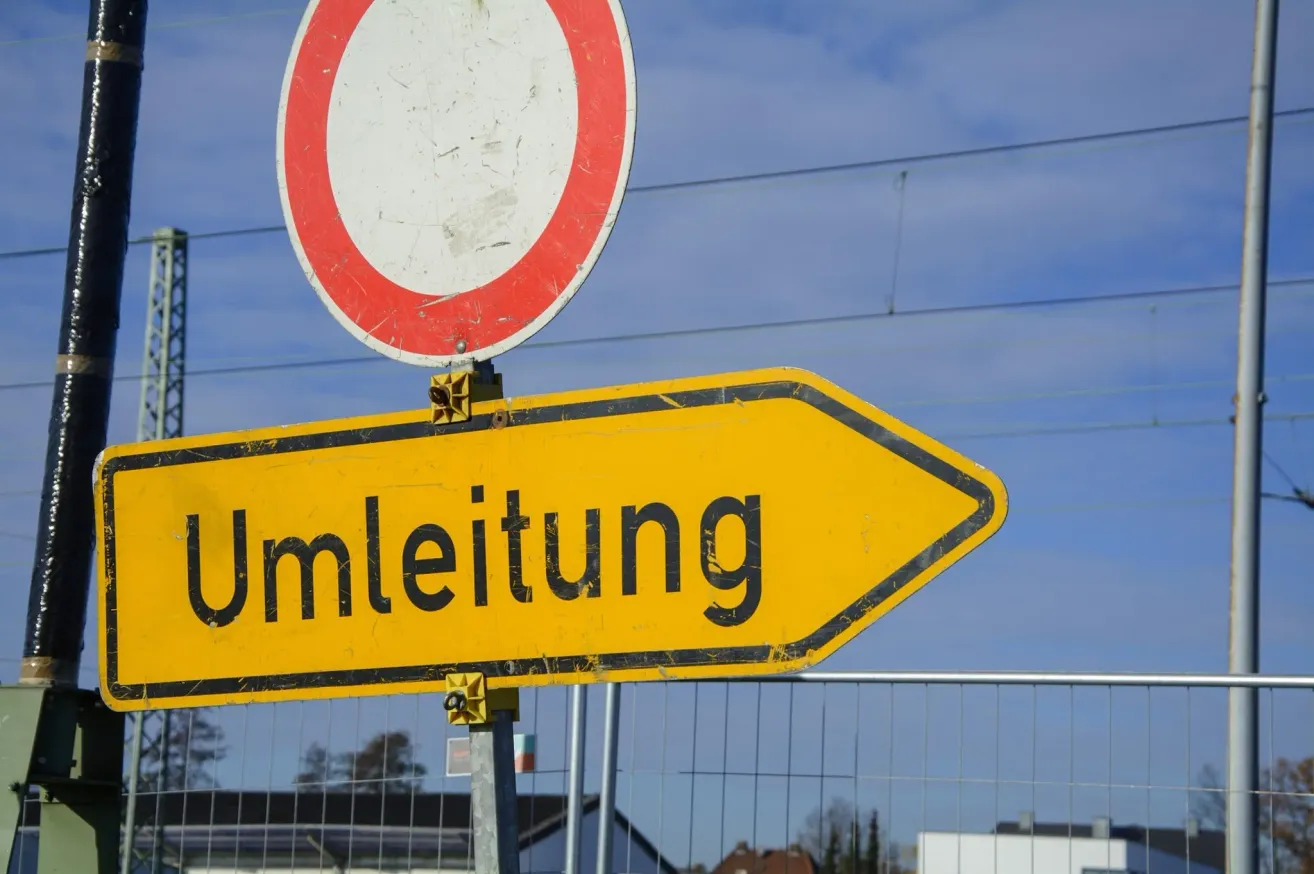 Ein gelbes Straßenschild mit dem Wort 'Umleitung' in schwarz, das eine Umleitung anzeigt. Darunter befindet sich ein rotes und weißes kreisförmiges Schild.