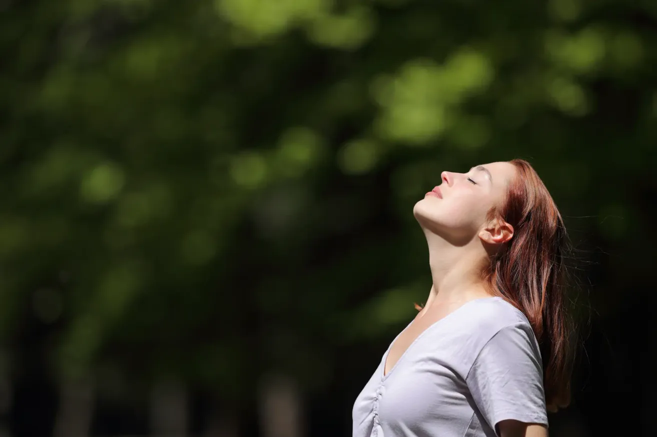 A woman with red hair looks up at the sky, her eyes closed and mouth slightly open. She is wearing a white shirt.