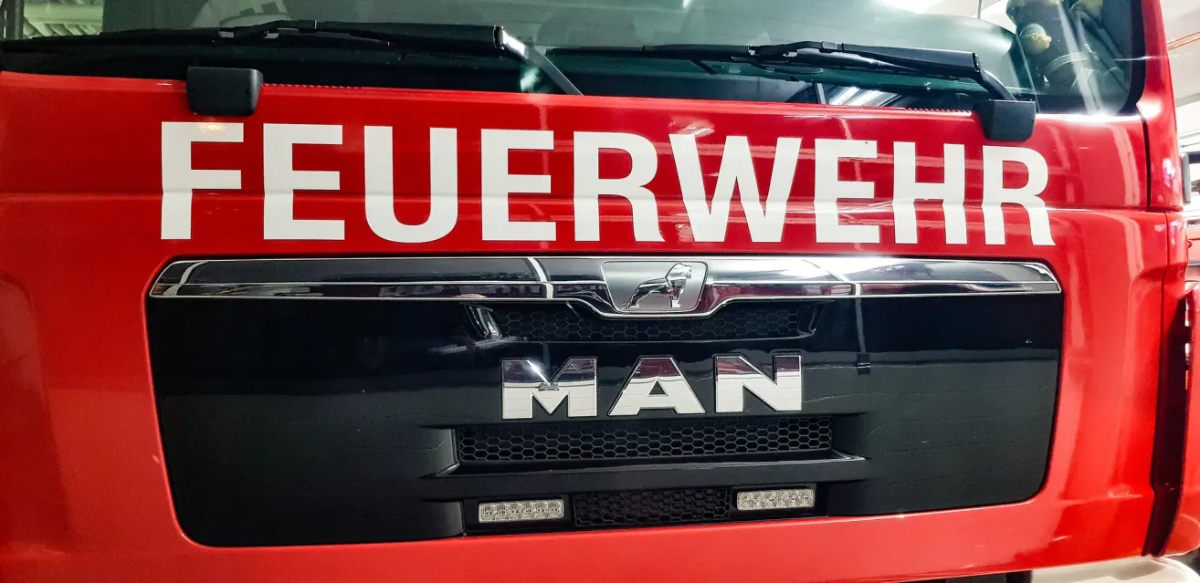 Close-up of a red MAN fire truck with 'FEUERWEHRE' written in white on the front. The front grill and headlights are visible.