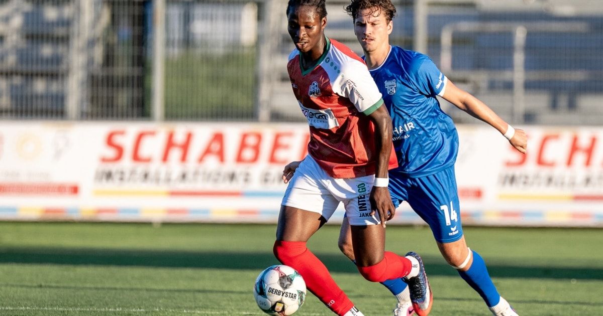 Zwei Fußballspieler auf dem Feld, einer in Rot und Weiß, der andere in Blau, beide konzentrieren sich auf den Ball.