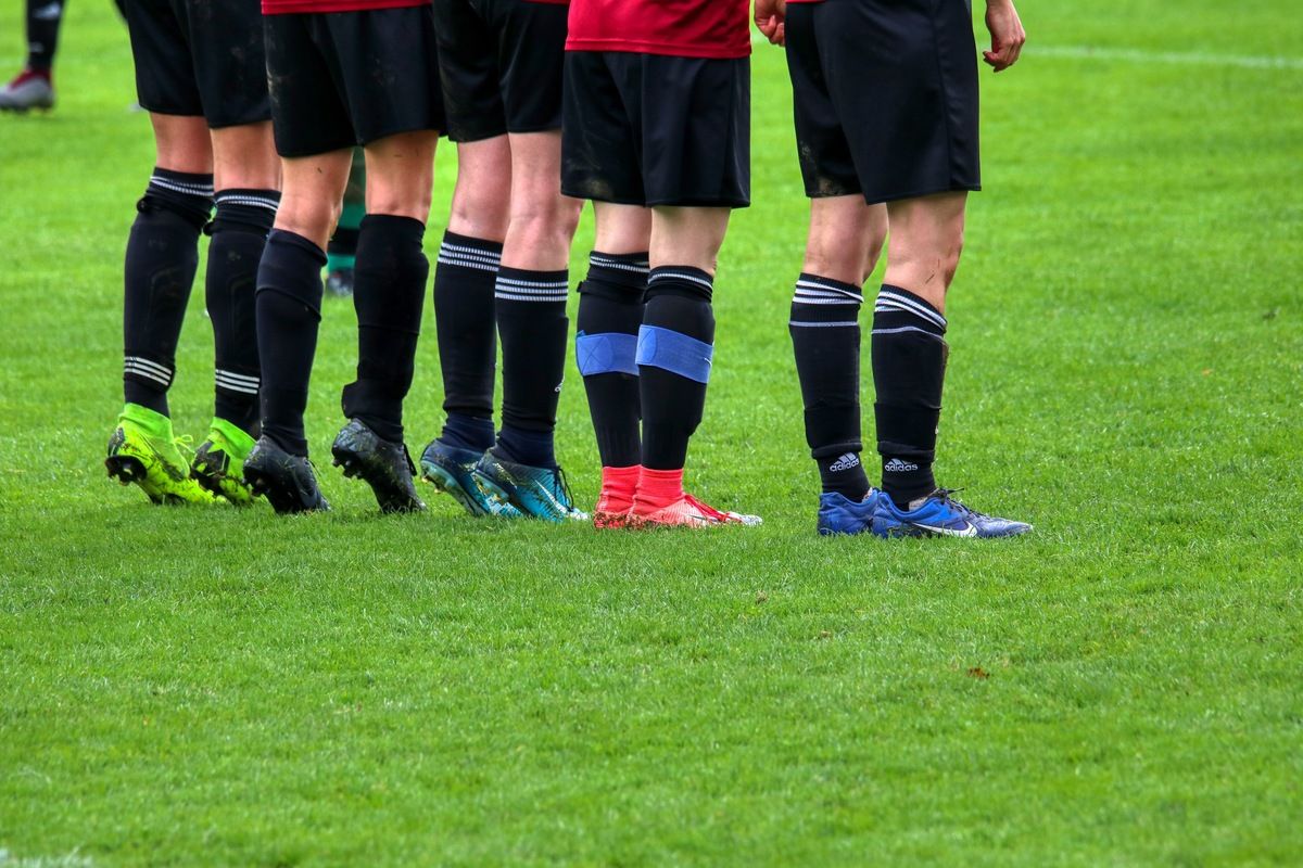 Eine Gruppe von Fußballspielern in schwarzen und roten Uniformen steht auf einem grünen Feld, ihre Beine und Schuhe sichtbar.