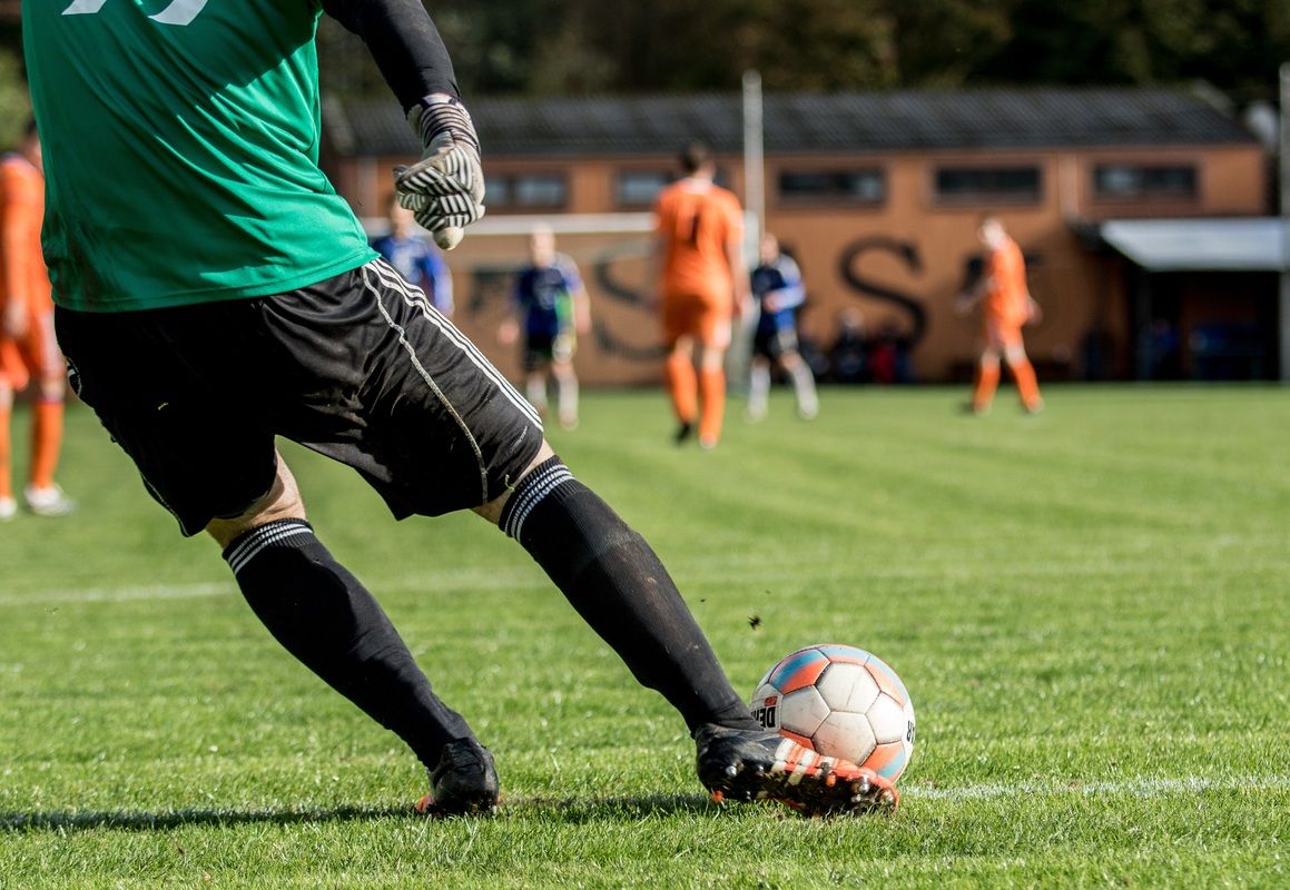 Ein Fußballspieler in einem grünen Trikot steht kurz davor, den Ball auf einem Rasenfeld zu schießen.