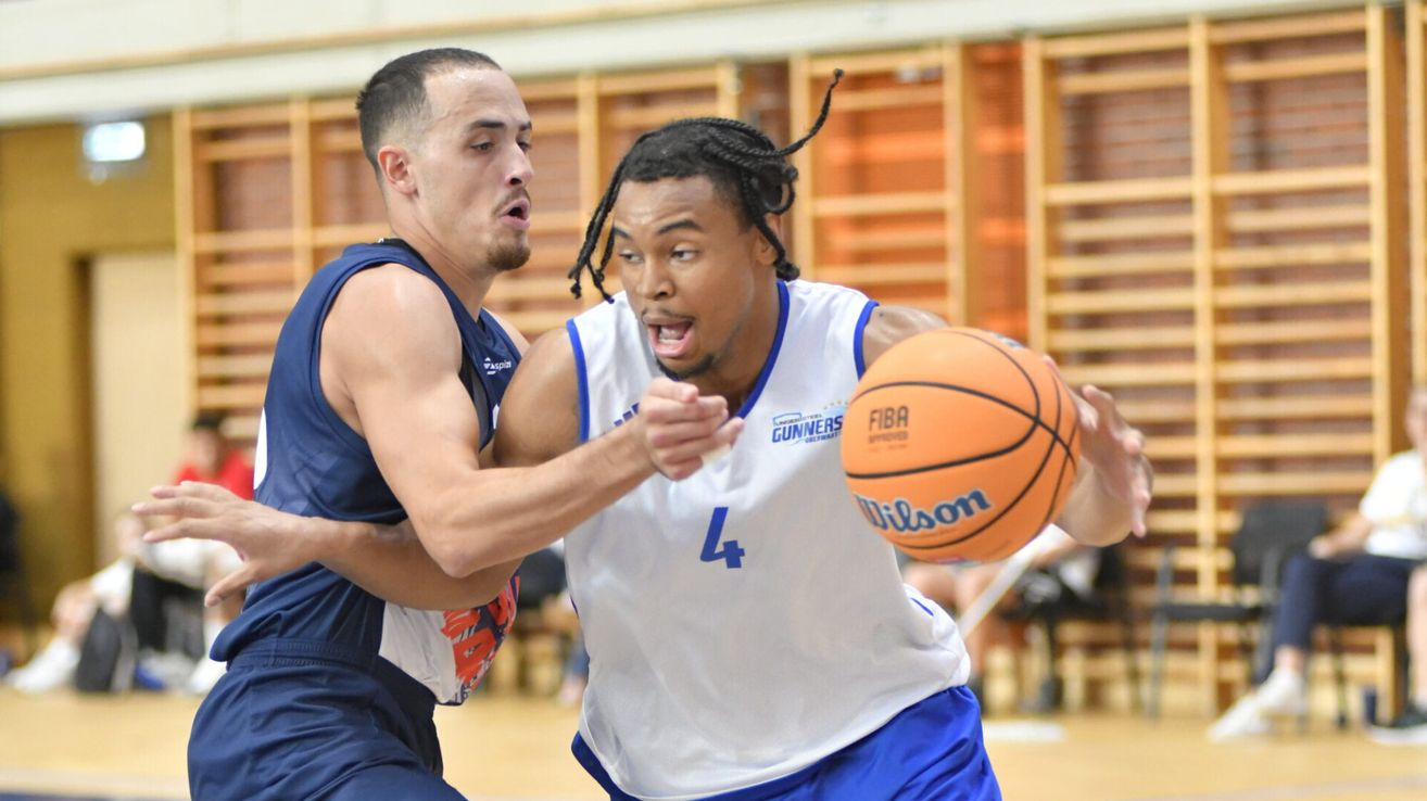 Two basketball players are in a heated match, one in a white jersey with the number 4 and the other in a blue jersey. They are both focused on the ball.