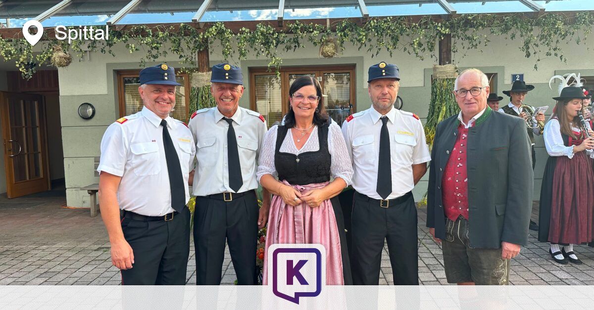 Fünf Personen in Uniformen und traditioneller Kleidung stehen vor einem Gebäude mit dekorativen Pflanzen.