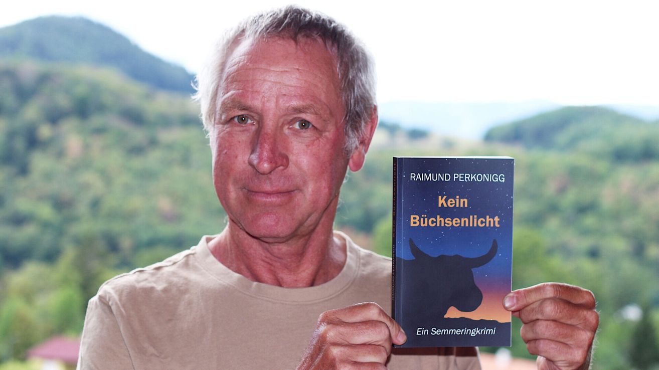 An older man with gray hair holds up a book titled 'Kein Buchsenlicht' with a bull silhouette on the cover.