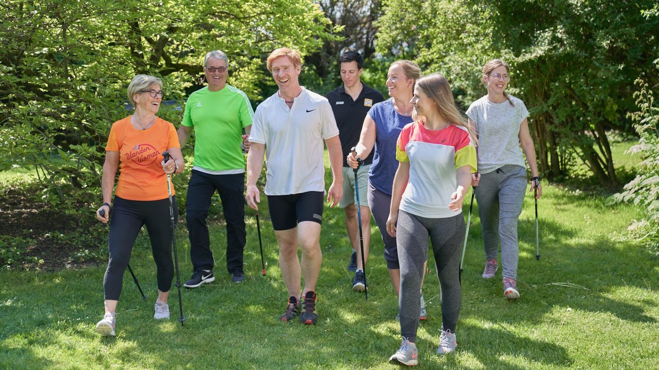 A group of people are walking in a park with walking sticks, wearing various colored shirts and sneakers.