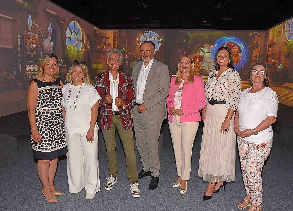 Eine Gruppe von Menschen, darunter Männer und Frauen, stehen zusammen vor einer großen Leinwand. Sie alle lächeln und scheinen für ein Foto zu posieren.