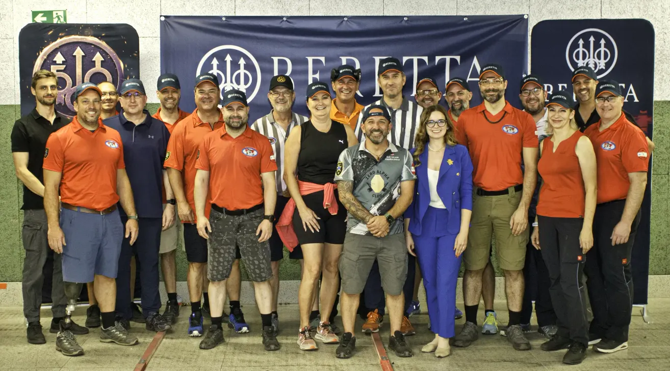A group of people dressed in orange and black, standing in front of a banner with the word Beretta. They are smiling and posing for a photo.