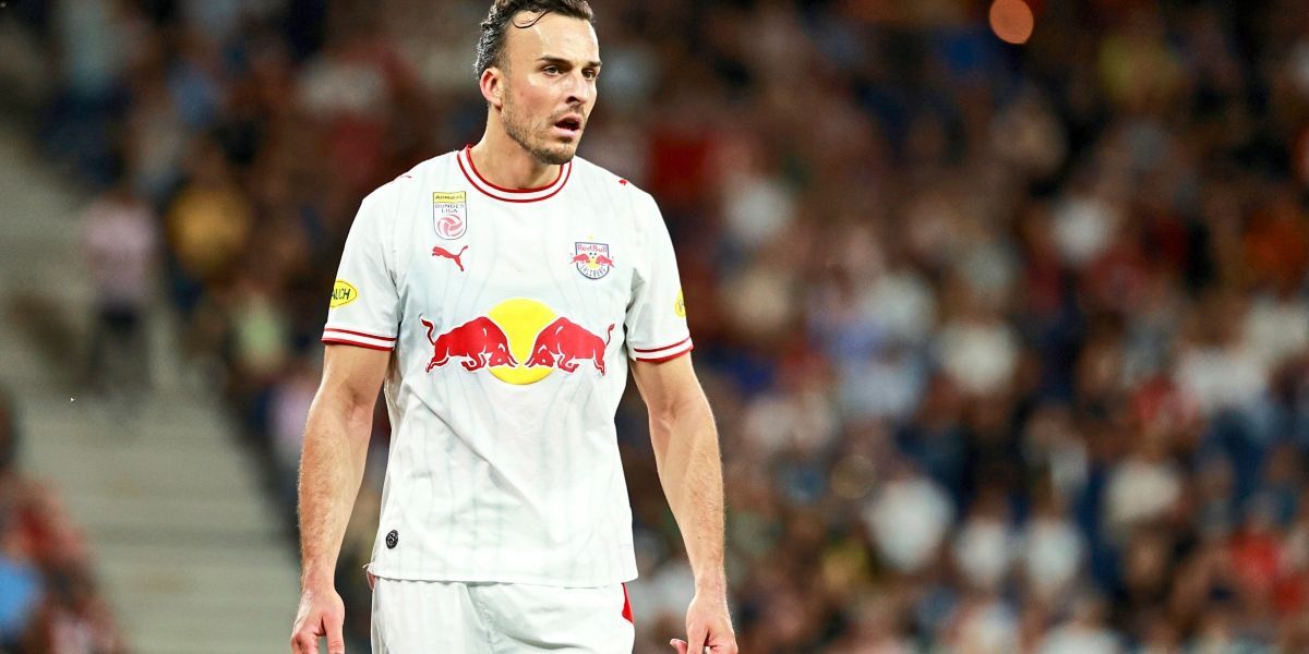 Ein Fußballspieler in einem weißen Trikot mit roten Akzenten und einem roten Bullenlogo auf der Brust, läuft auf dem Feld.