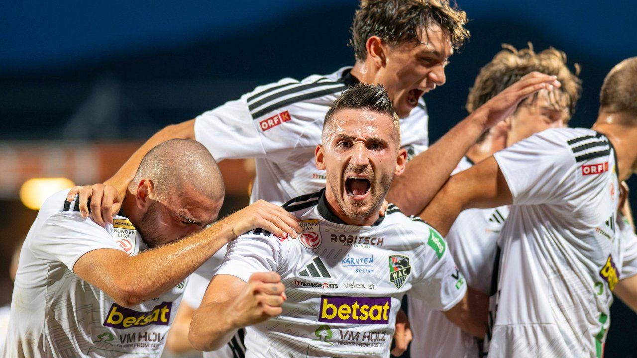 Eine Gruppe von Fußballspielern feiert einen Sieg, wobei ein Spieler in der Mitte schreit.