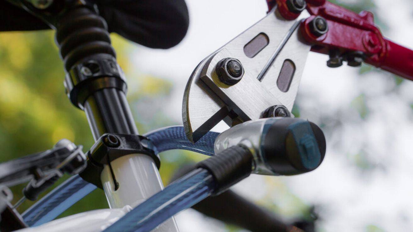 Ein Nahaufnahme einer Fahrradbremsanlage, die die Metallbremszangen und hydraulischen Bremsleitungen zeigt. Der Fahrradrahmen ist teilweise sichtbar, mit einem blauen Kabel, das durch ihn verläuft.