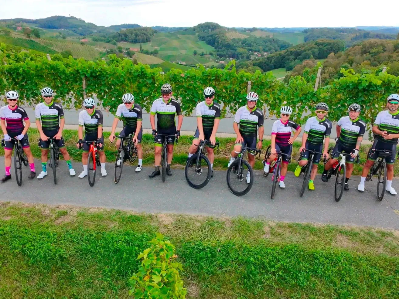 Eine Gruppe von Radfahrern in passenden Uniformen posiert für ein Foto in einem Weinberg mit einer malerischen Kulisse.