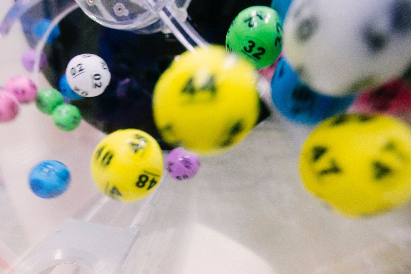 A close-up view of various colored dice, including yellow, green, and purple, with numbers and symbols on them, suspended in the air.