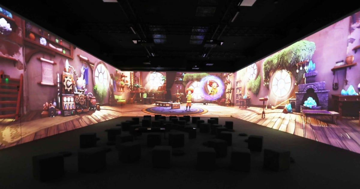 Ein immersives Theater mit einer großen Leinwand, die eine farbenfrohe Animationsszene mit zwei Charakteren zeigt. Der Raum ist dunkel, und das Publikum sitzt auf schwarzen Kissen.