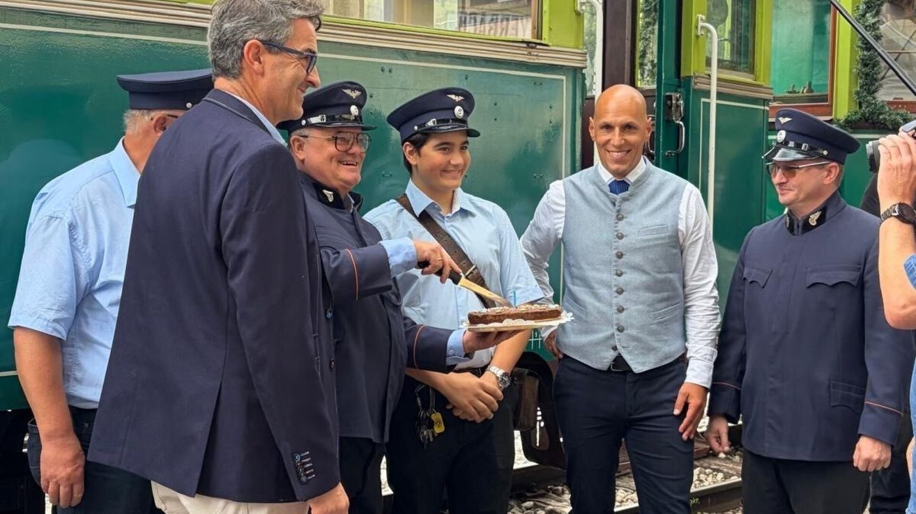 Three men in uniforms and one in a suit celebrate with a cake on a train platform.