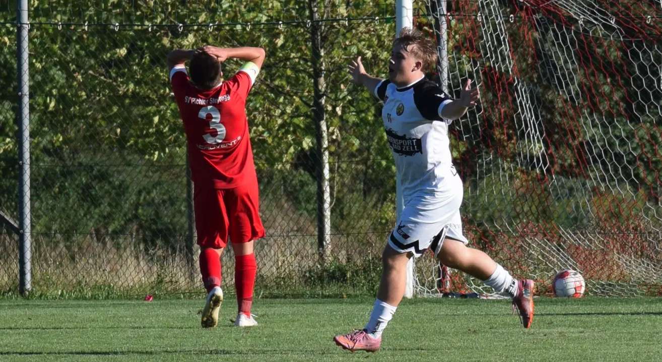 Ein Fußballspieler mit der Nummer 3 auf seinem roten Trikot hält sich die Hände vors Gesicht. Ein anderer Spieler in einem weißen Trikot läuft auf das Tor zu.