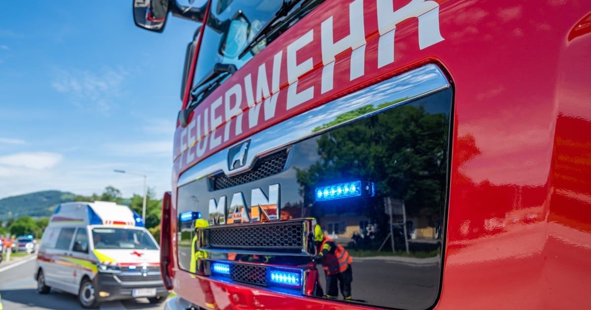 A red fire truck with the word 'Feuerwehr' on the front, parked on the side of the road with blue lights on.