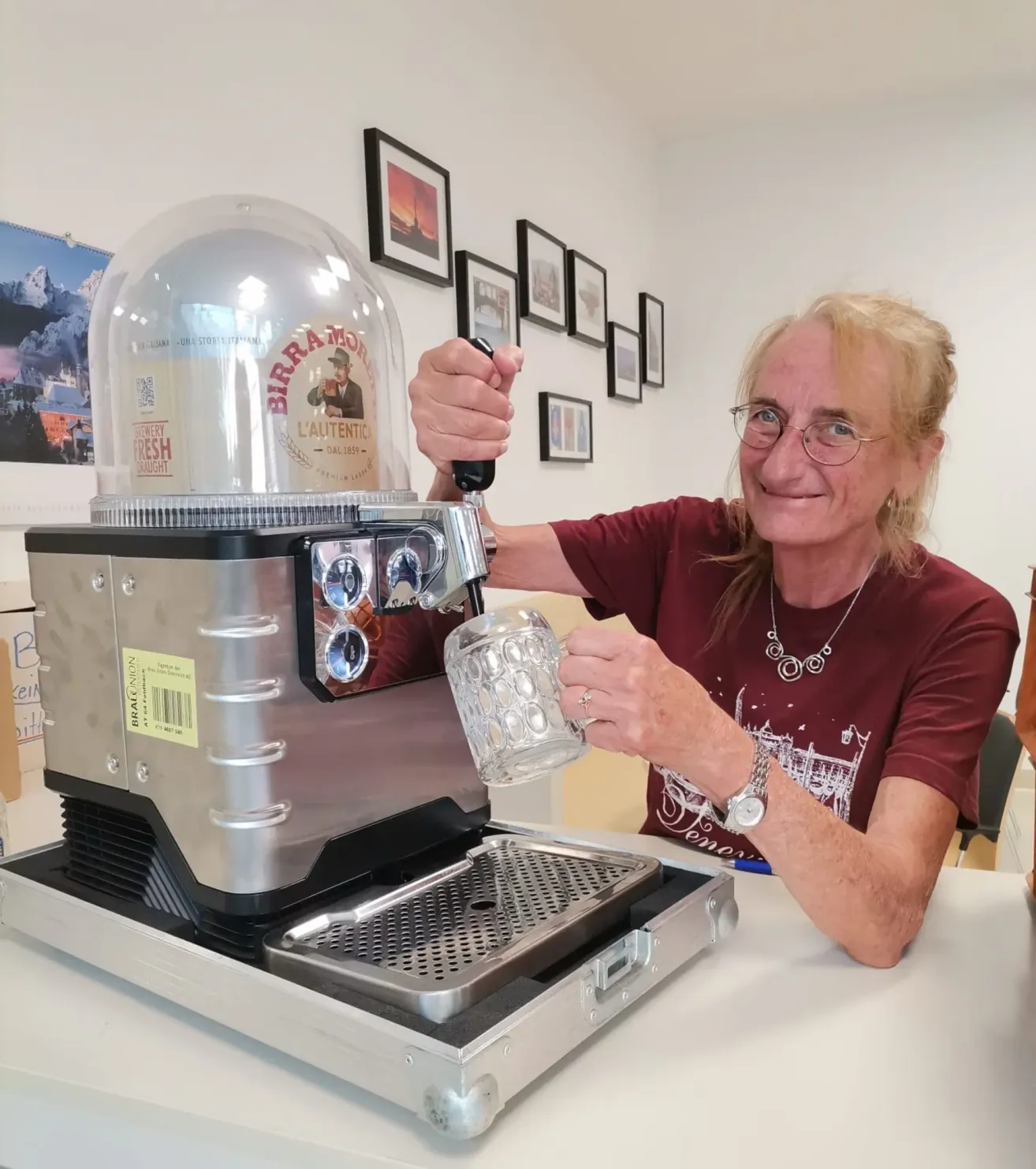 An elderly woman with glasses is pouring a glass of beer from a beer tap machine. She is smiling and seems to be enjoying the moment.