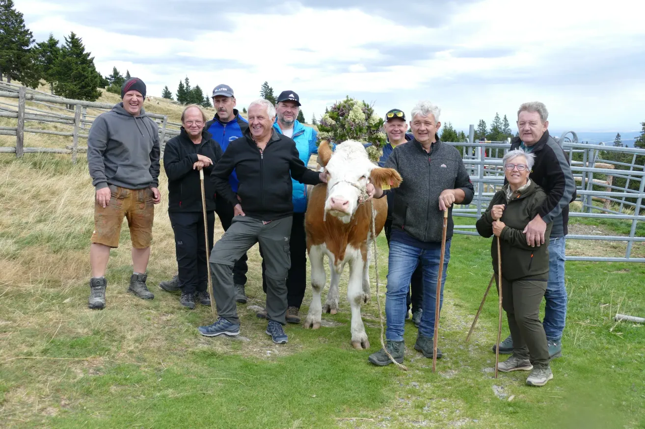 Eine Gruppe von Menschen, darunter ein Mann, der eine Kuh hält, steht auf einem Feld mit einer Kuh in der Mitte.
