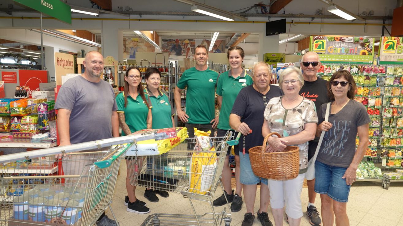 A group of people, likely employees, stand in a store with shopping carts and baskets. They are all wearing green uniforms.