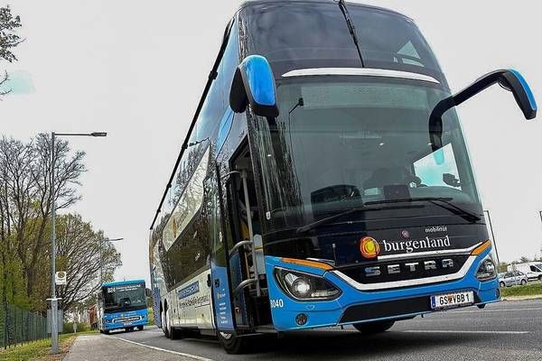 A blue double-decker bus with the word Burgenland on the front is parked on the side of the road. Another bus is driving on the road.