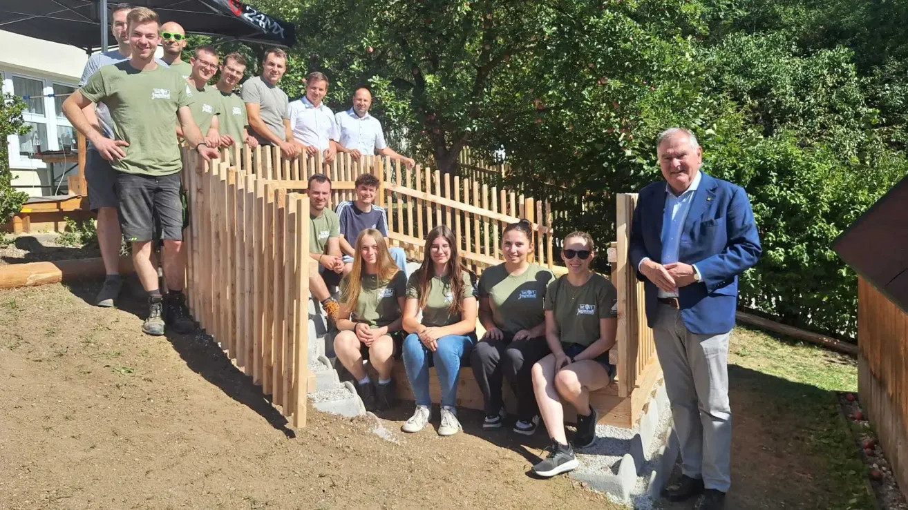 A group of people in green shirts are posing for a photo on a wooden structure with a man in a blue suit standing nearby.