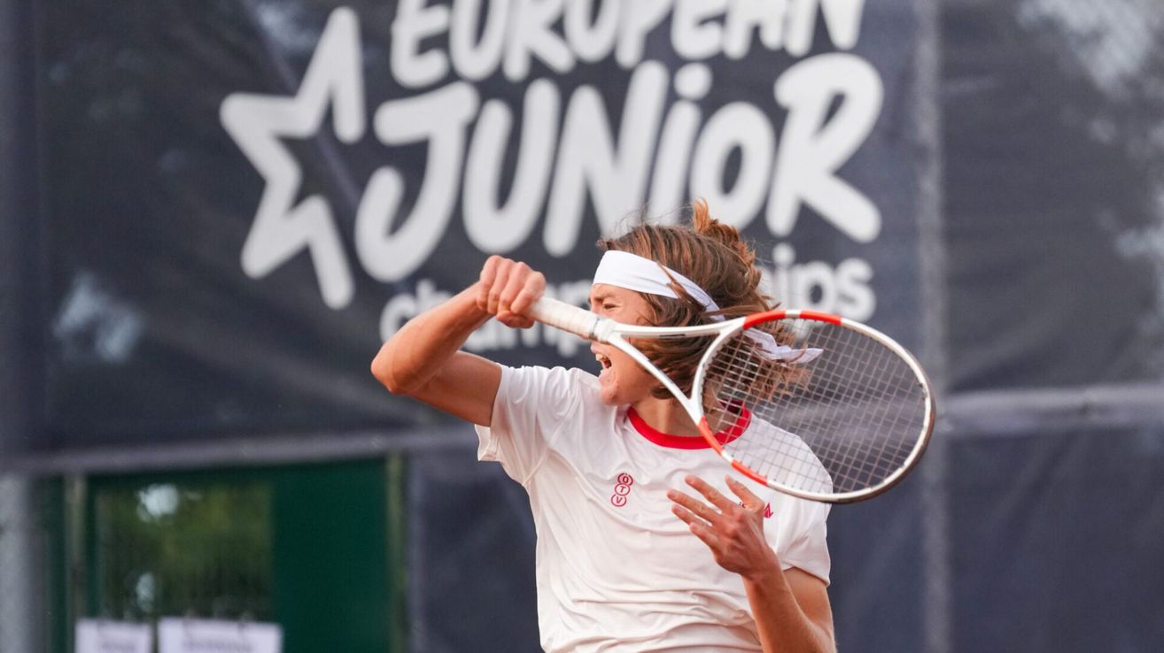 Ein junger Tennisspieler in einem weißen Shirt und Stirnband schreit, während er während eines Matches einen Tennisschläger schwingt.