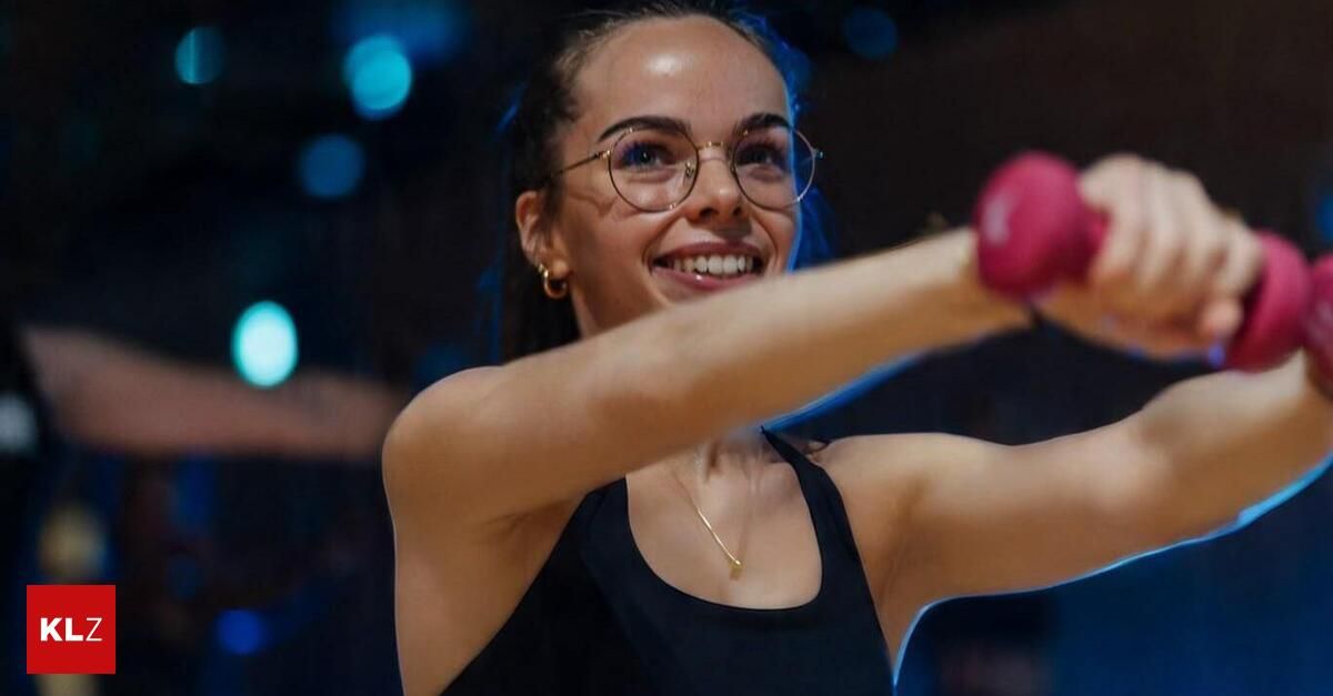 Eine Frau mit blauen Haaren, die eine schwarze Tanktop und eine rosa Boxhandschuh trägt, lächelt.