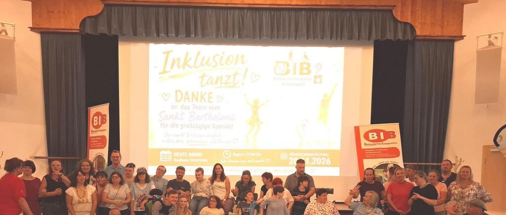 Eine Gruppe von Menschen versammelt sich in einem Raum mit einer Projektionsleinwand, auf der 'Inklusion tanzt!' und 'DANKE' steht. Sie lächeln und scheinen eine Veranstaltung zu genießen.