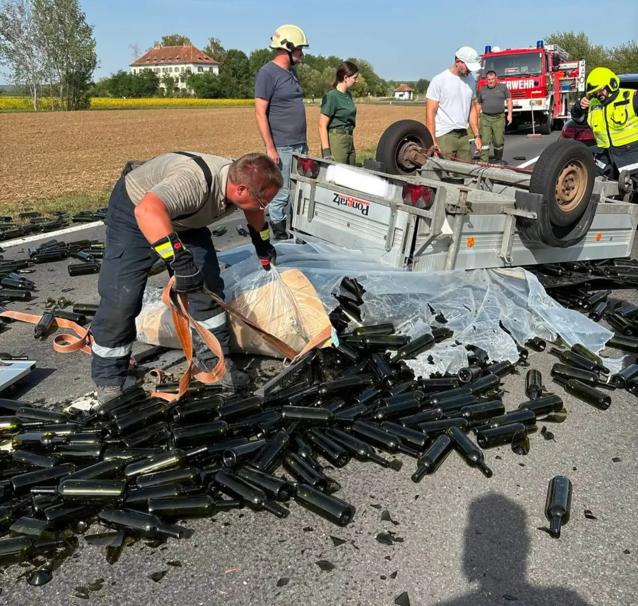 Ein Mann in einer Warnweste sammelt zerbrochene Flaschen von der Straße nach einem LKW-Unfall.