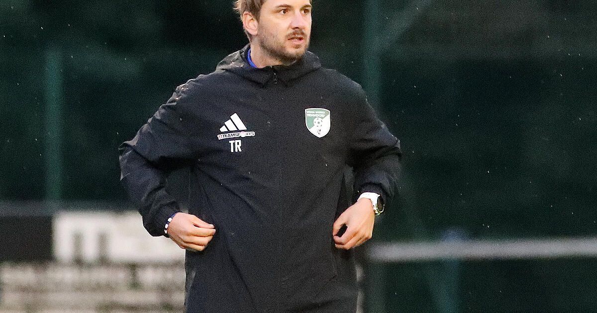 A man in a black Adidas hoodie with a white logo on the left chest and a white logo on the right chest is running on a field.