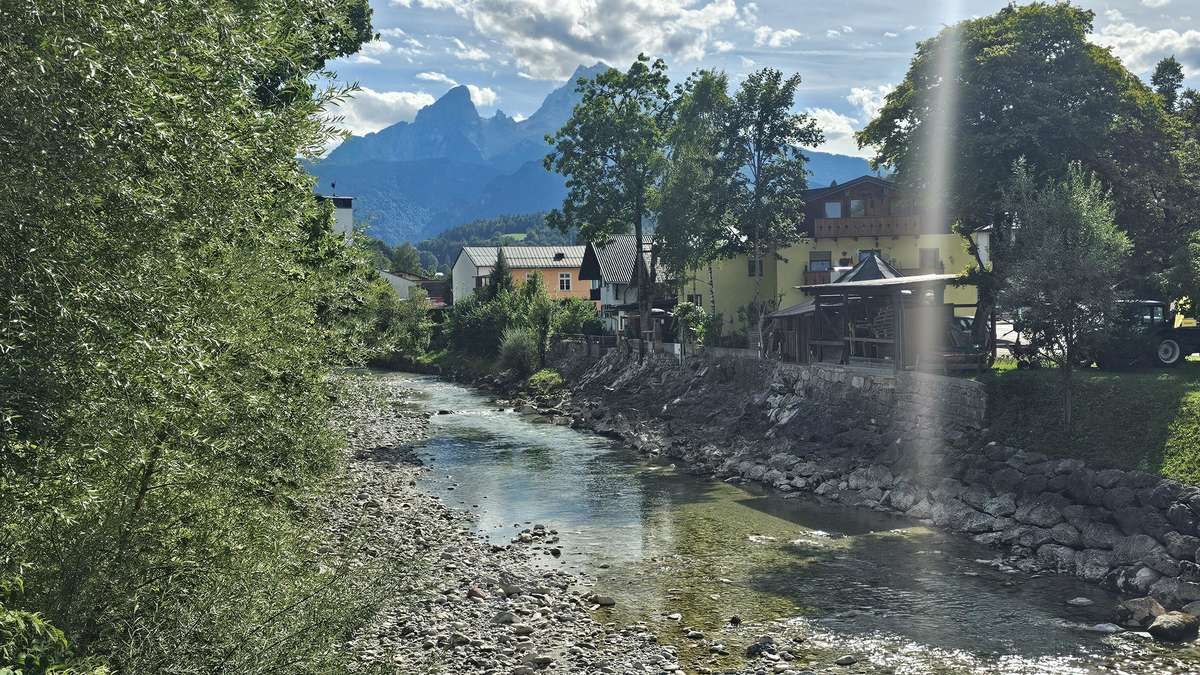 Ein Fluss fließt durch eine Stadt mit Bergen im Hintergrund, umgeben von Bäumen und Gebäuden.