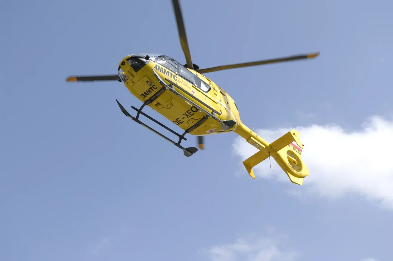 Ein gelber Hubschrauber mit der Aufschrift DAMTC und DE-XEQ an der Seite fliegt am Himmel.