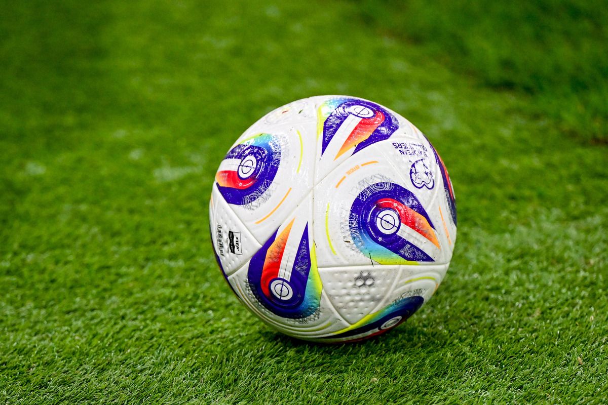 A soccer ball with a multicolored design is resting on a green grass field. The ball has a white base with various colorful patterns and logos.