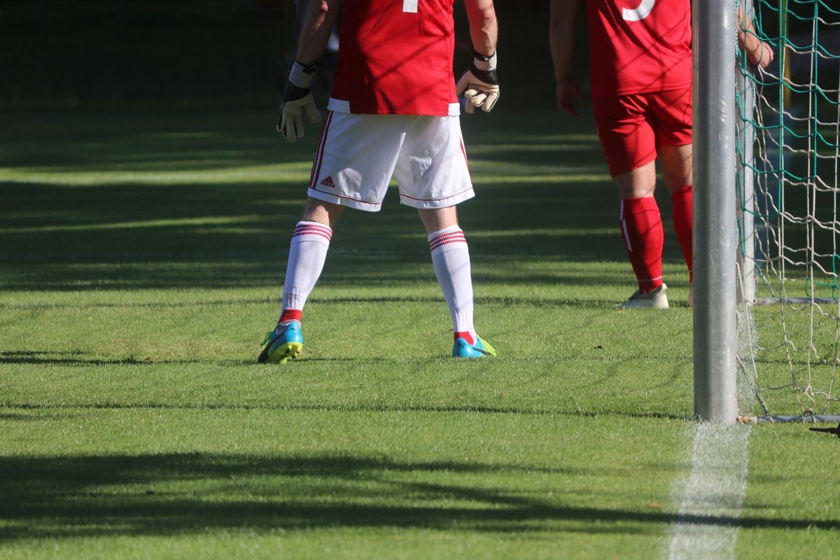 Zwei Fußballspieler in roten Trikots und weißen Shorts stehen auf einem Feld. Der Spieler vorne hat die Nummer 1 auf dem Rücken.