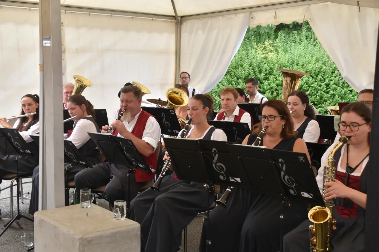 Eine Gruppe von Musikern in traditioneller Kleidung spielt Instrumente in einem Zelt, mit einer Kulisse aus Grün.