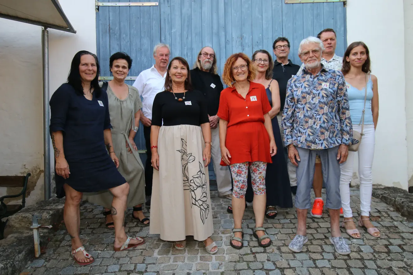 Eine Gruppe von Erwachsenen, sowohl Männer als auch Frauen, stehen zusammen vor einer blauen Holztür und lächeln für ein Foto.