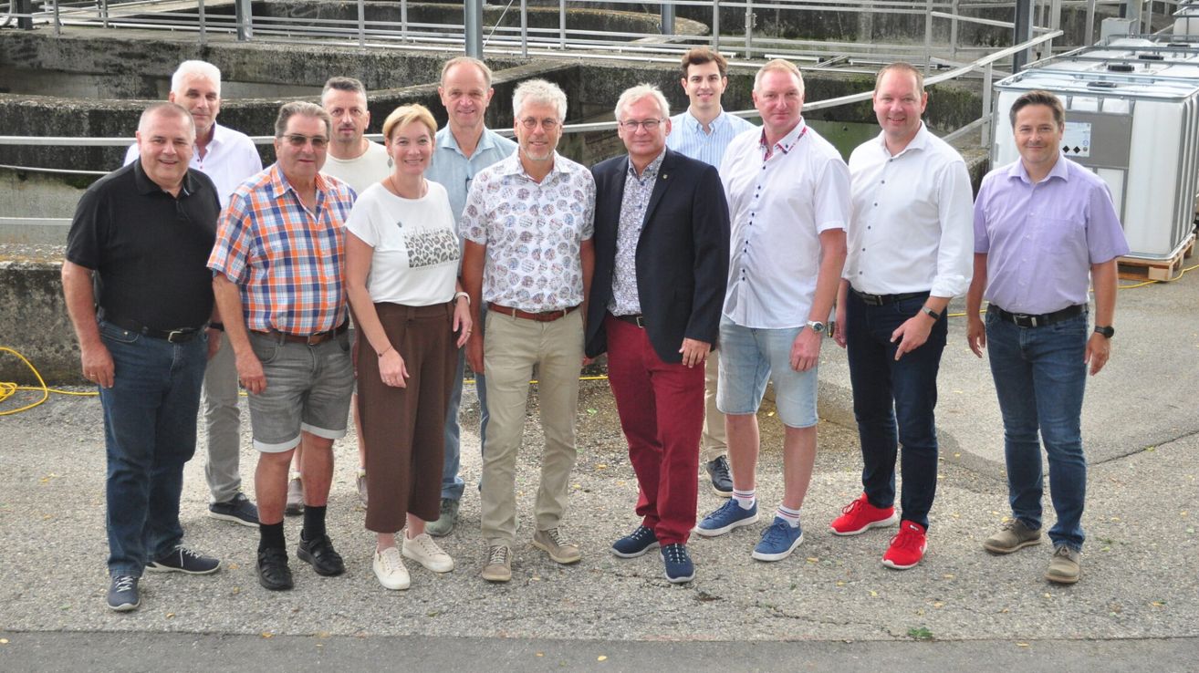 A group of people, possibly colleagues, standing in front of a concrete structure with a metal railing. They are all smiling and appear to be posing for a photo.