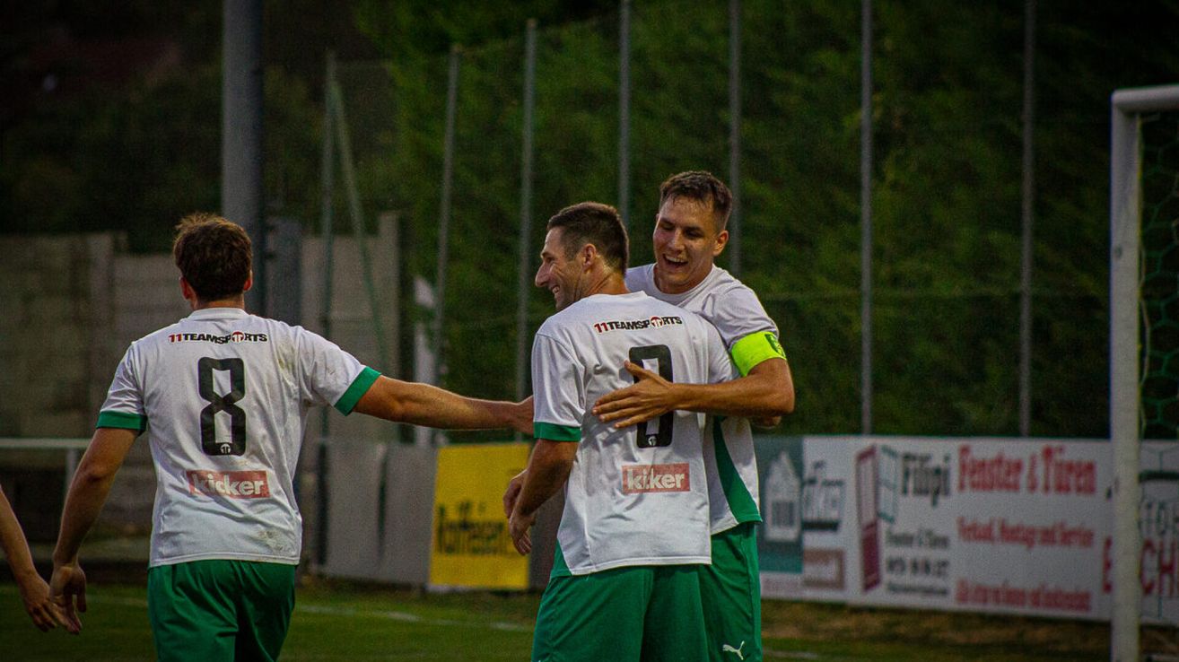 Zwei Fußballspieler in grünen und weißen Trikots feiern ein Tor auf einem Feld bei Nacht.