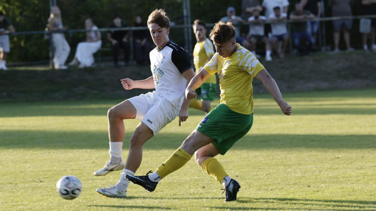 Zwei Fußballspieler in Aktion auf einem Feld, einer in Weiß und Schwarz und der andere in Gelb und Grün. Sie befinden sich in einer Wettkampfstellung, wobei ein Spieler versucht, den Ball zu stehlen.