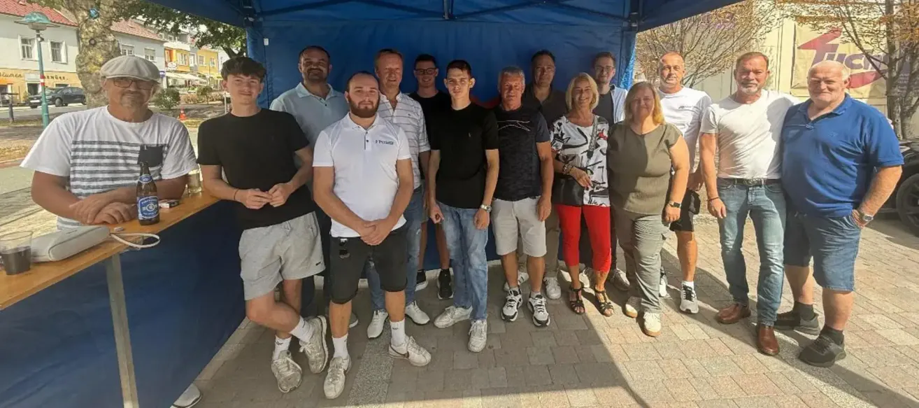 Eine Gruppe von Menschen, sowohl Männer als auch Frauen, stehen unter einem blauen Zelt und lächeln für ein Foto.