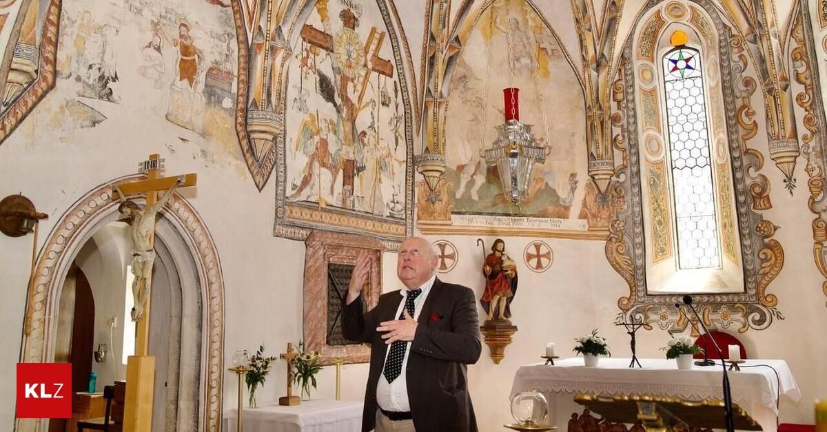 Ein älterer Mann in einem Anzug steht in einer Kapelle und gestikuliert mit den Händen. Die Kapellenwände sind mit religiösen Gemälden und einer Statue geschmückt. Ein Kerze und Blumen stehen auf dem Altar.