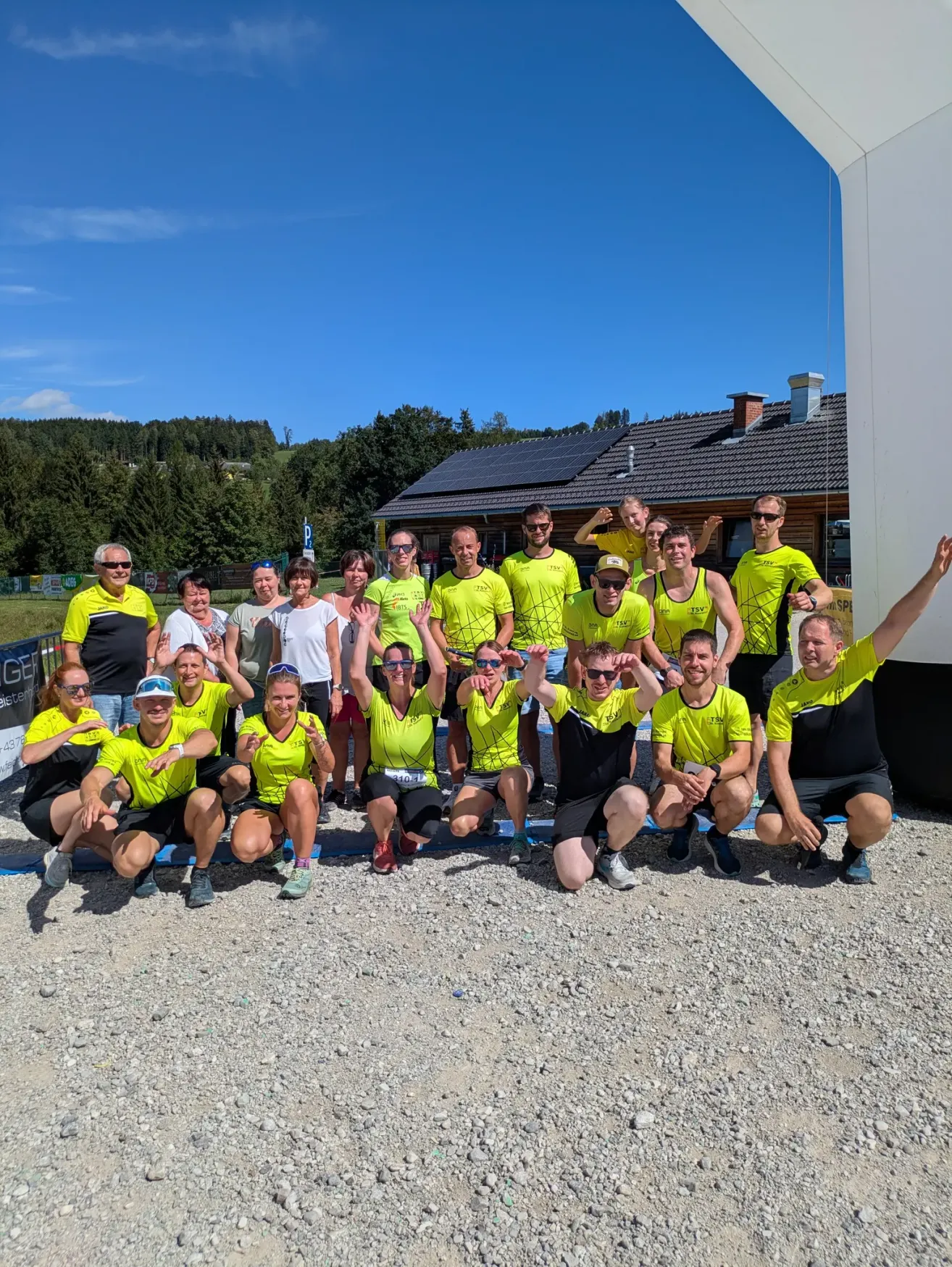 Eine Gruppe von Menschen in gelber und schwarzer Sportbekleidung posiert für ein Foto vor einem Gebäude mit Solarmodulen auf dem Dach.